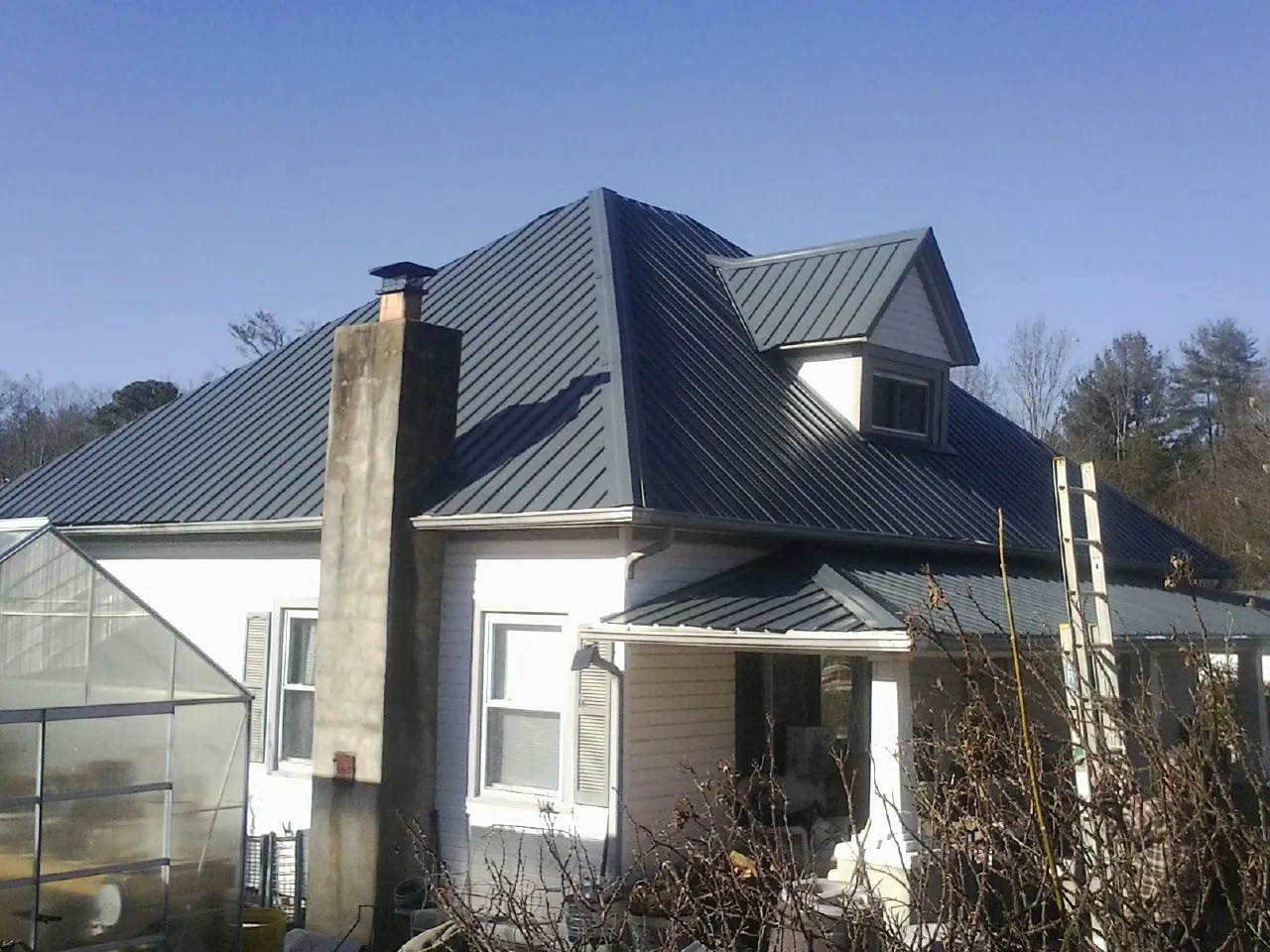 Dark blue standing seam metal roof on a white farmhouse with dormer — Slate & Tile Roof Repair by Roofing Brothers in New Brighton