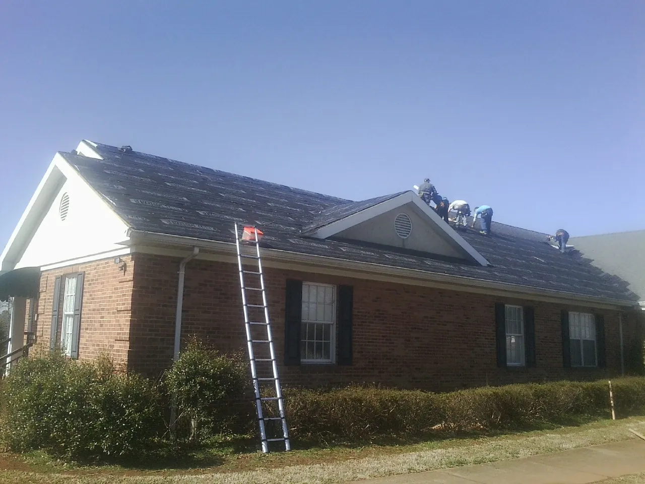 Crew tearing shingles off a brick ranch roof with a ladder set — Metal Roof Repair work by our crew in New Brighton