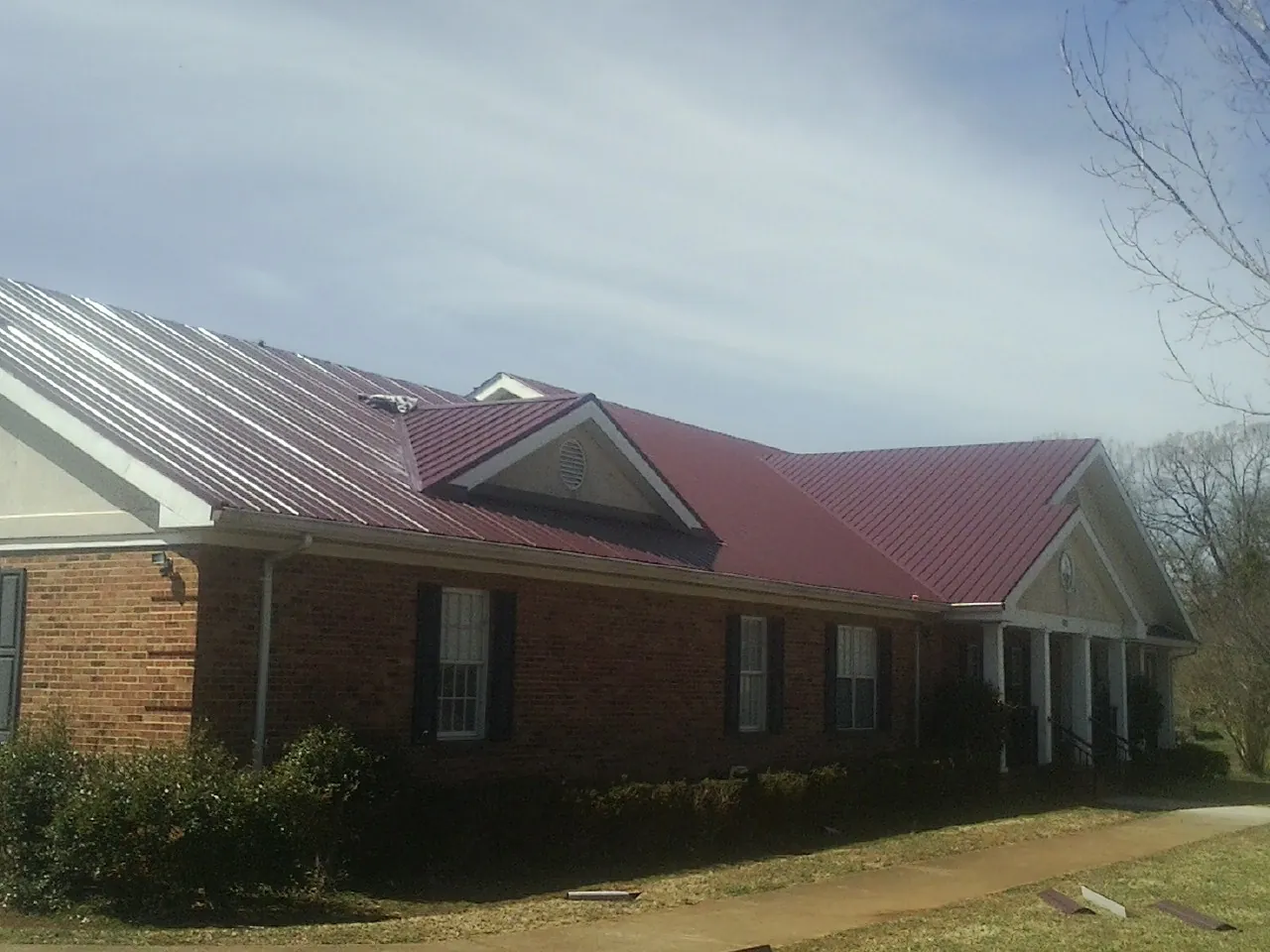 Red metal roof with gabled entries on a long brick building, from a Hail Damage Roof Repair job in New Brighton