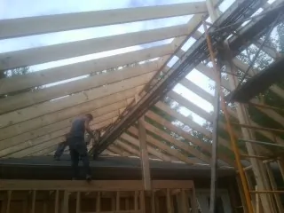 Rafters going up over a new addition with a worker on the wall in New Brighton
