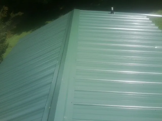 New green metal panels meeting at the ridge of a roof — Flat Roof Repair work by our crew in New Brighton