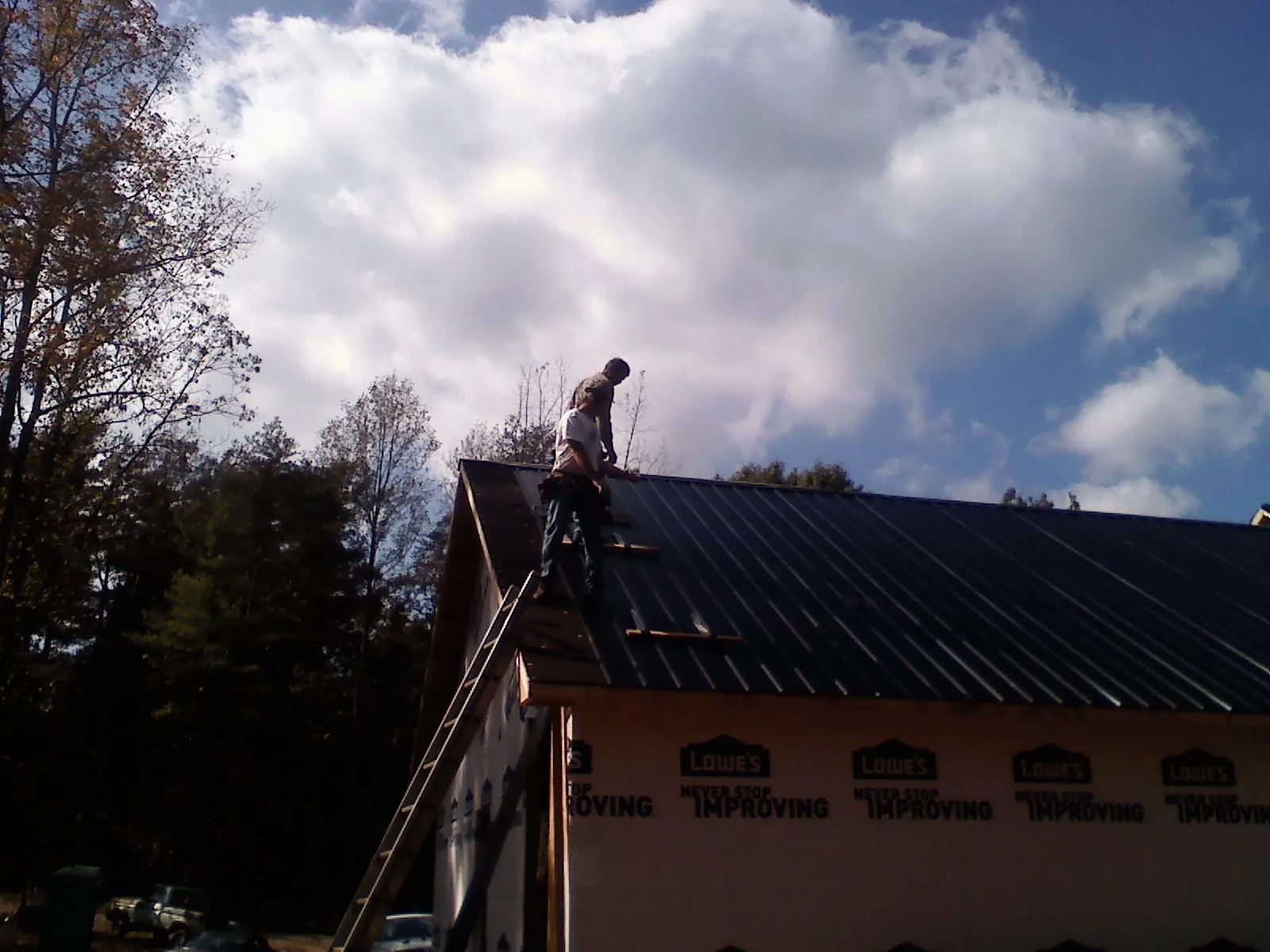 Roofer fastening dark metal panels high against a cloudy sky, from a Roof Inspection job in New Brighton