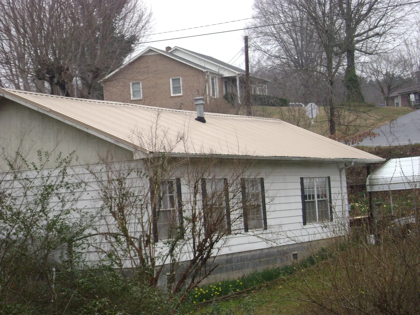 Tan metal roof on a white sided house set into a hillside — Commercial Roofing by Roofing Brothers in New Brighton